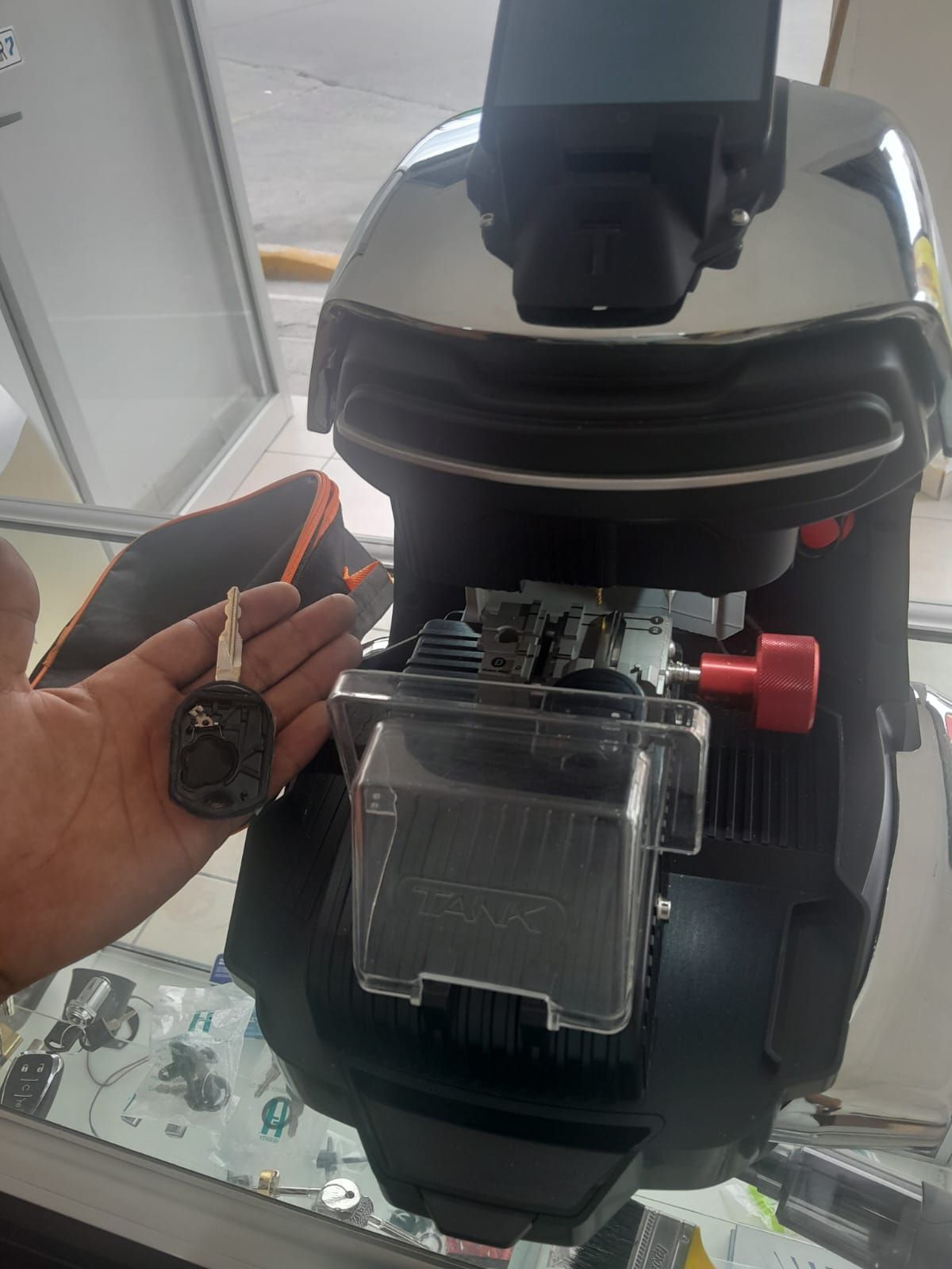 Mano sosteniendo una llave de coche junto a una duplicadora. La máquina es negra y tiene un pomo rojo.