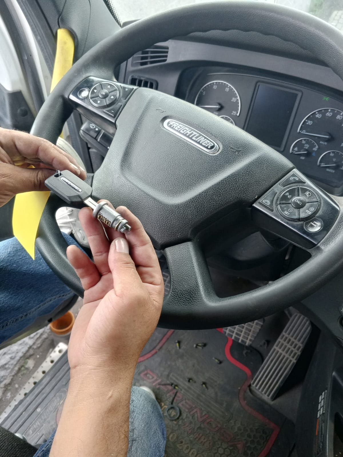 Persona sosteniendo una llave de camión y el encendido, cerca de un volante de Freightliner dentro de la cabina de un camión.