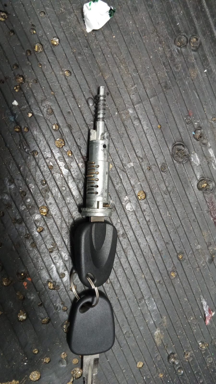 Cilindro de encendido de automóvil con llave y otro llavero, sobre una superficie negra texturizada.