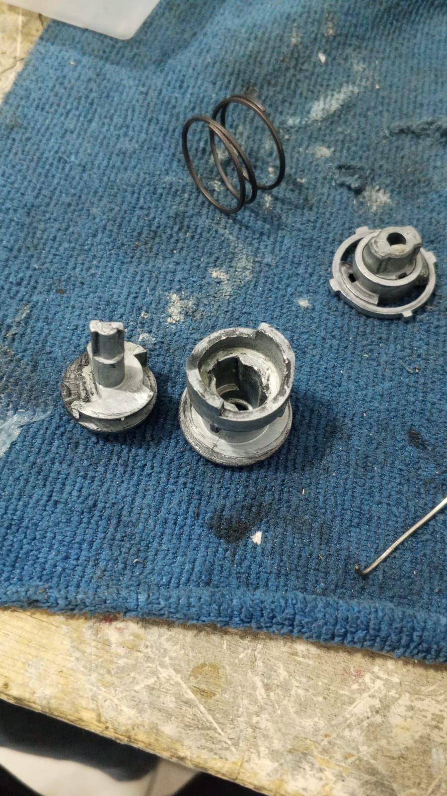 Piezas mecánicas desmontadas sobre un paño azul: carcasas cilíndricas, un resorte y otros componentes metálicos.