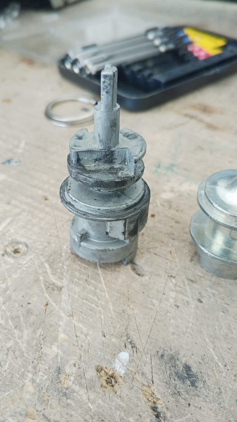 Primer plano de una cerradura de encendido de automóvil desmontada con un eje de llave y varios componentes sobre una superficie de madera.