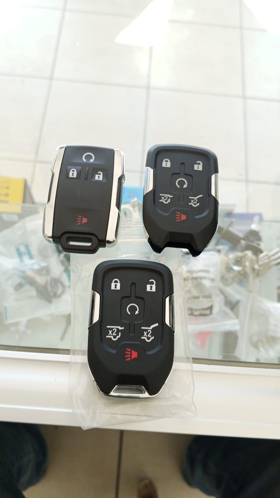 Tres llaveros de coche negros con detalles plateados sobre una superficie de azulejos.
