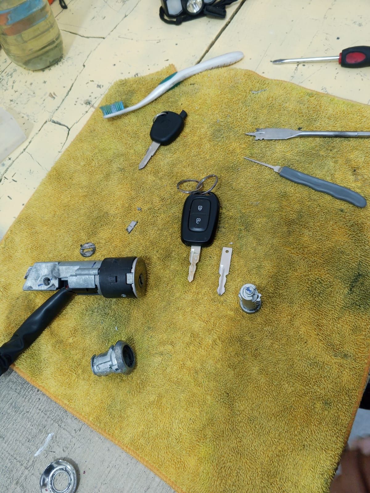 Piezas de encendido de automóvil desmontadas con llaves y herramientas sobre un paño amarillo.