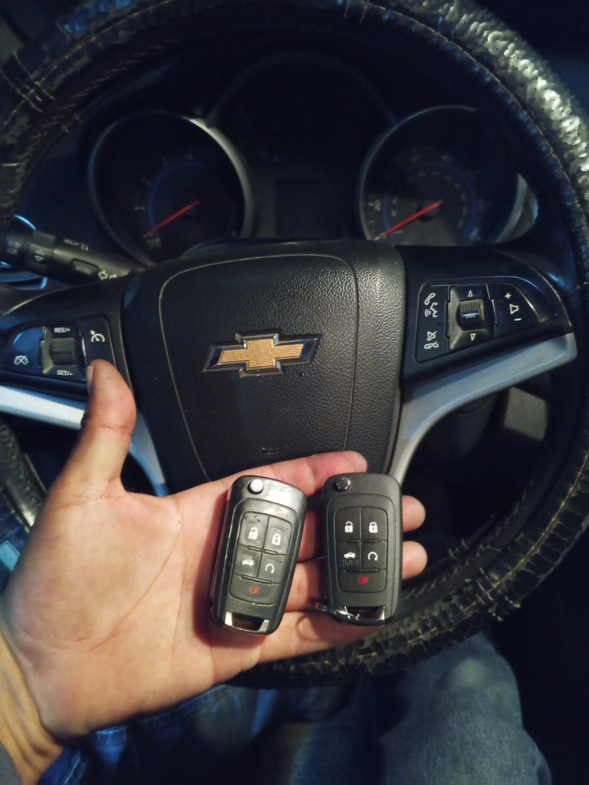 Persona sosteniendo dos llaves de coche delante del volante de un Chevrolet.