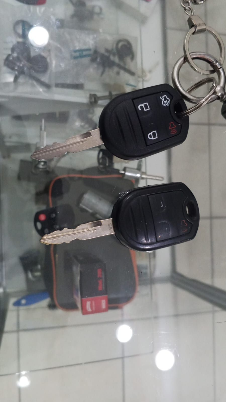 Dos llaves de coche negras con llaveros sobre una superficie reflectante.