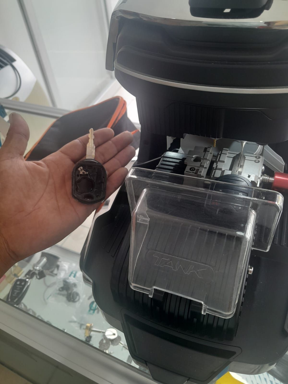 Mano sosteniendo una pequeña botella, cerca de un objeto desmontado con componentes de plástico transparente.