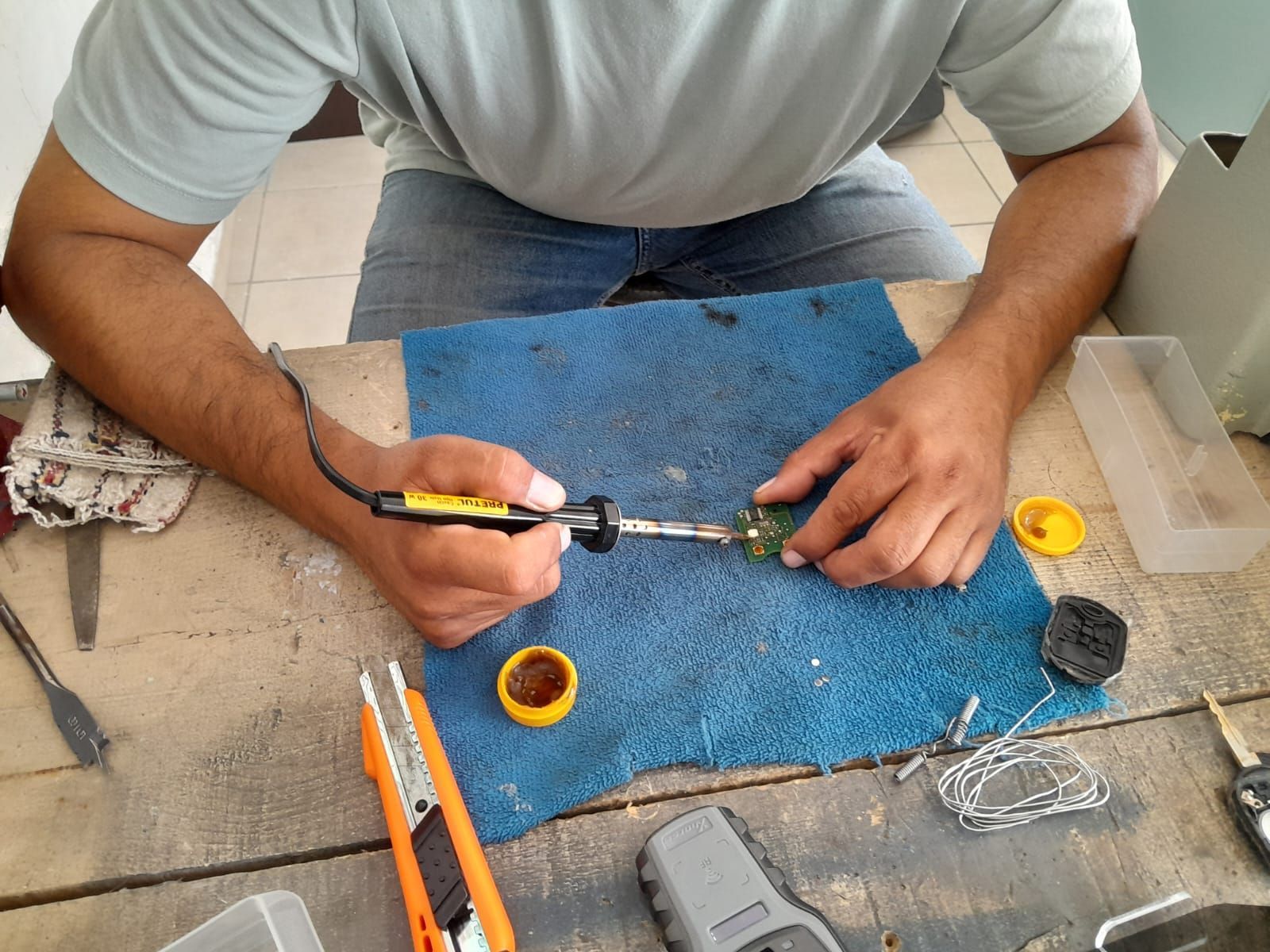 Persona soldando una placa de circuito sobre un paño azul en un banco de trabajo de madera.