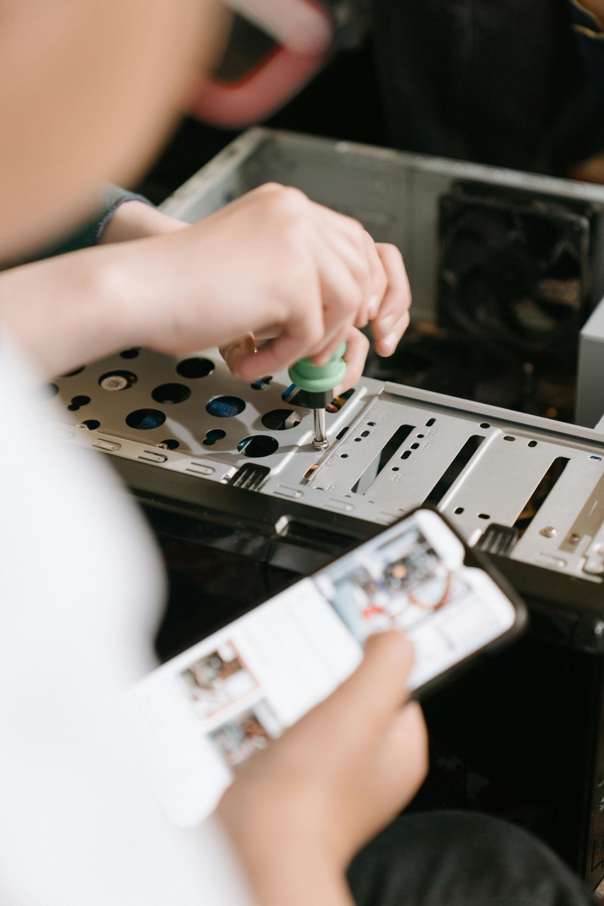 Person using a screwdriver to assemble a computer, holding a phone with instructions.