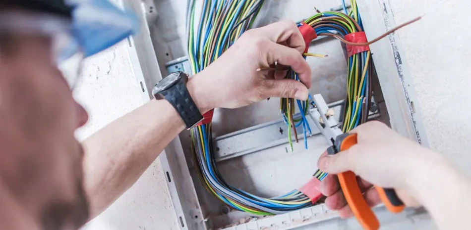 A man is working on an electrical box with a pair of pliers.