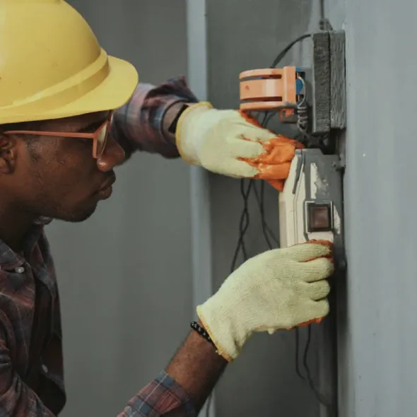 A man wearing a hard hat and gloves is working on an electrical box