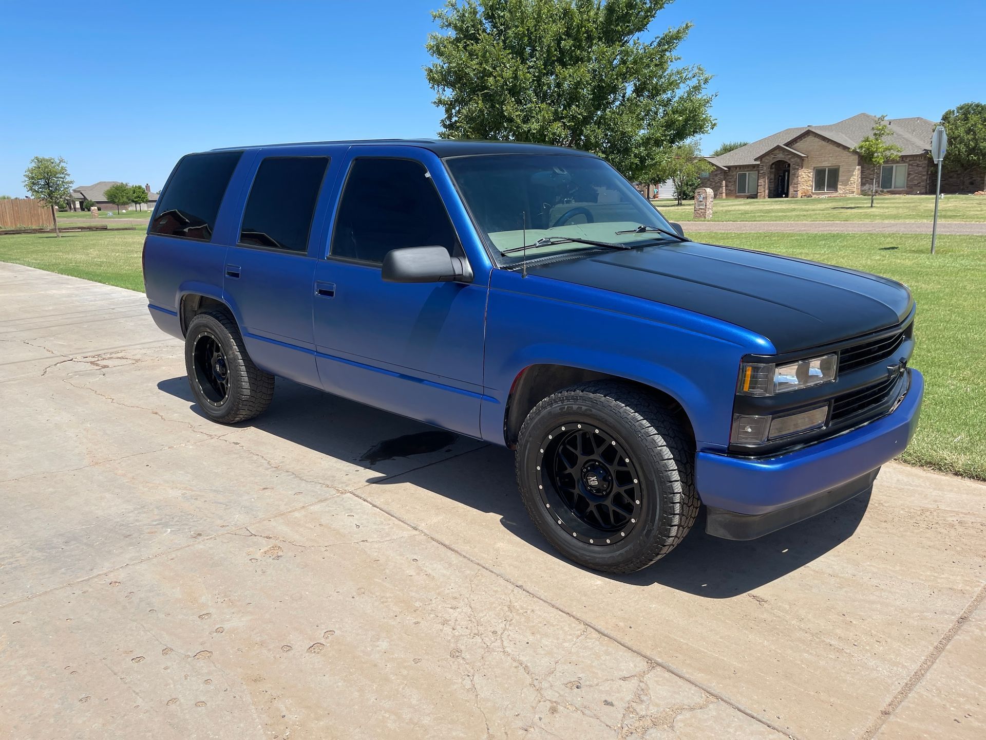 A blue suv is parked on a sidewalk in front of a house.