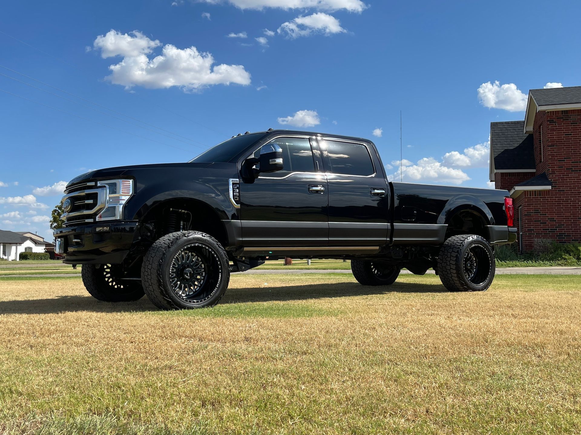 A black truck is parked in a grassy field in front of a brick building.