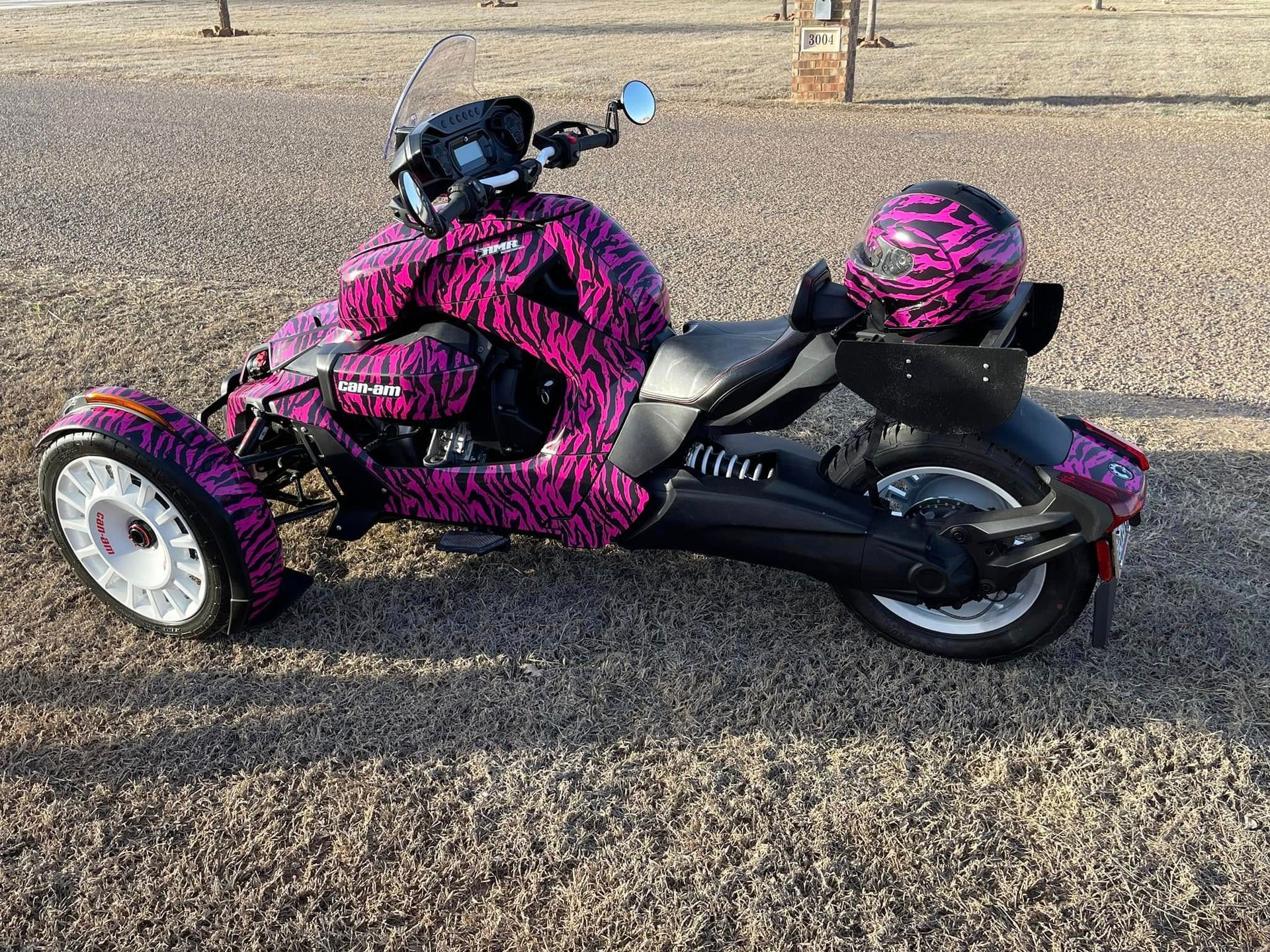 A pink and black motorcycle with three wheels is parked on the side of the road.