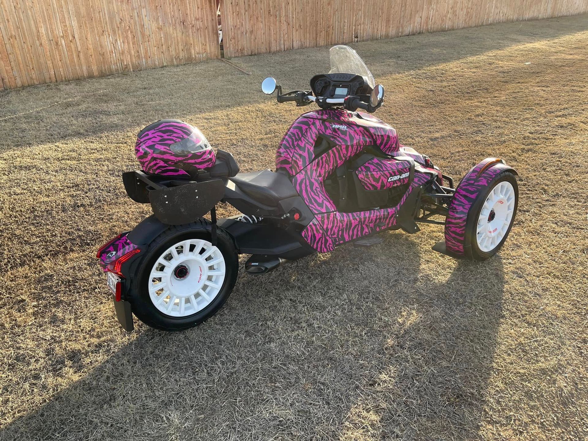 A pink and black motorcycle with a helmet on the back is parked on a gravel road.