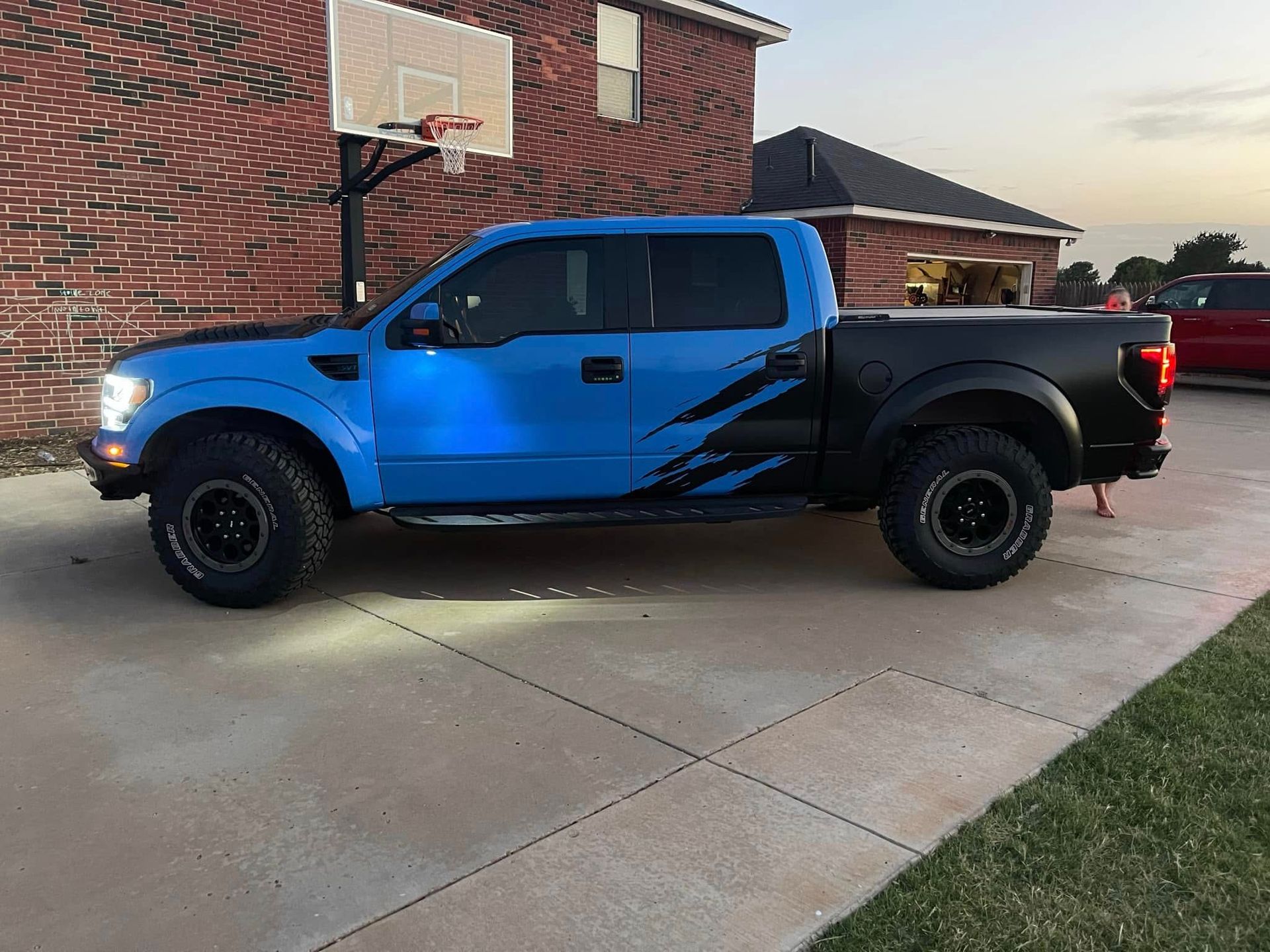 A blue and black truck is parked in a driveway in front of a brick building.