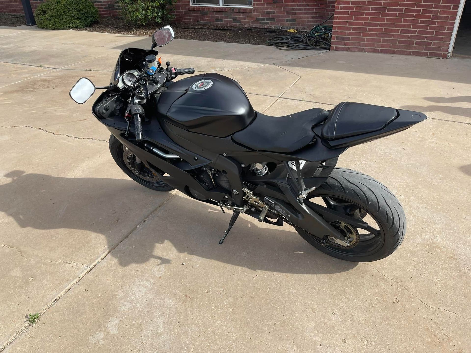 A black motorcycle is parked in a driveway in front of a brick building.