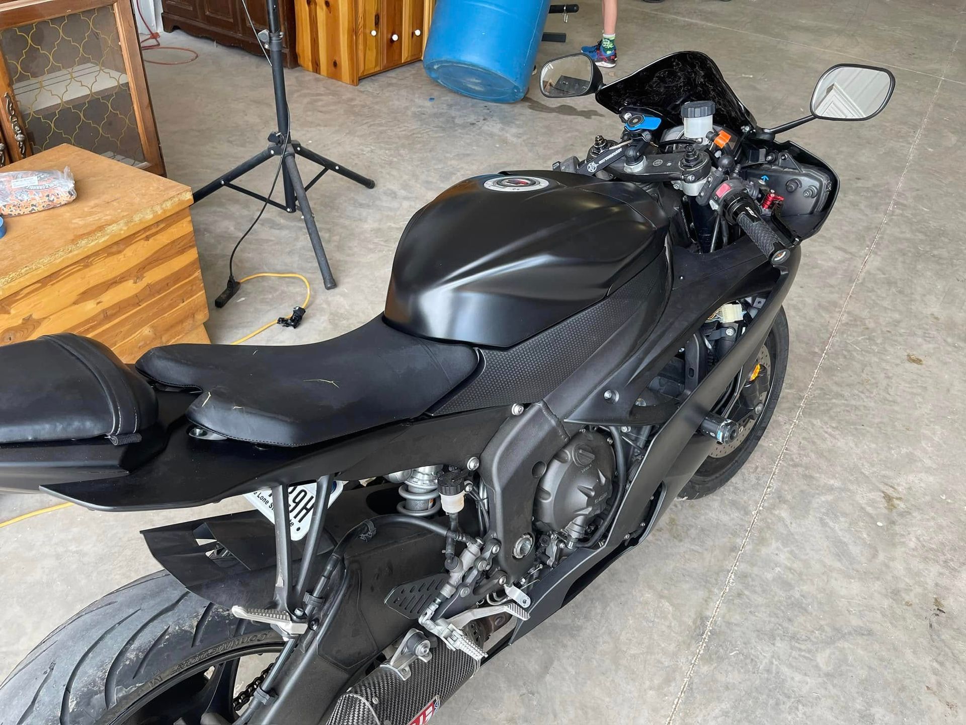 A black motorcycle is parked in a garage next to a blue barrel.