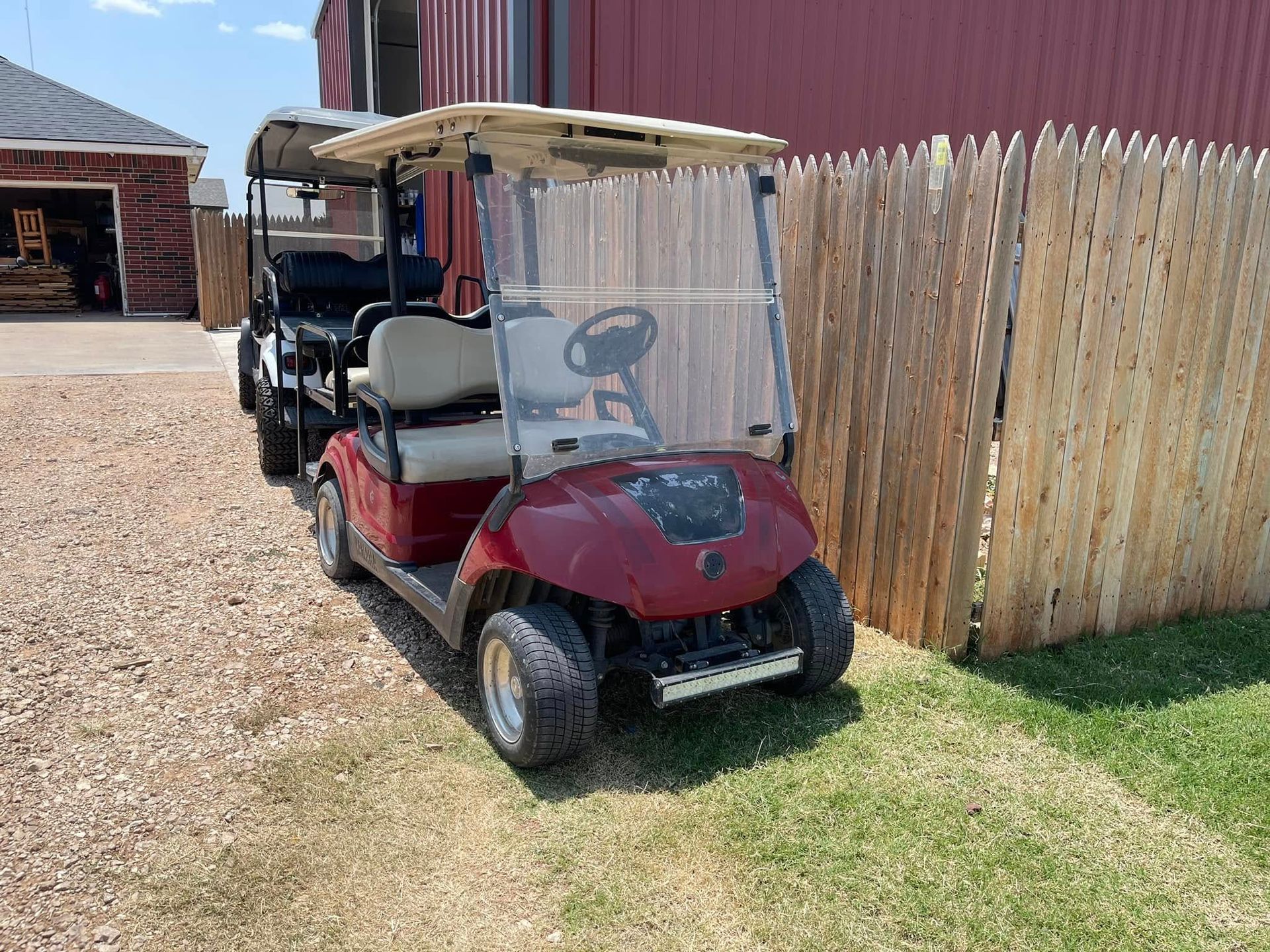 A red golf cart is parked in front of a wooden fence.