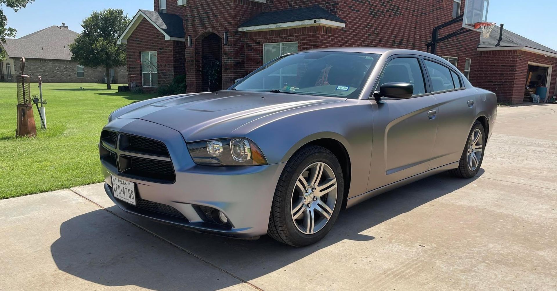 A gray dodge charger is parked in a driveway in front of a brick house.