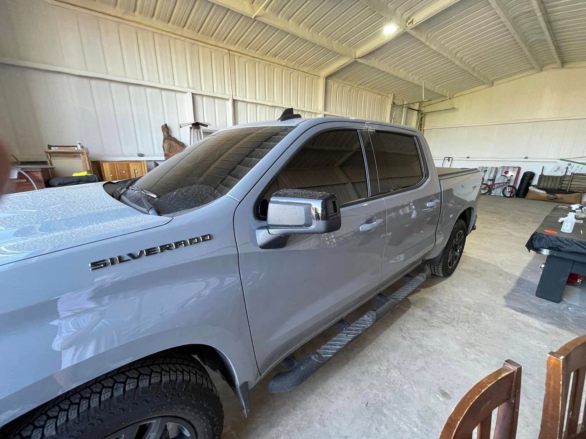 A silverado truck is parked in a garage next to a table and chairs.