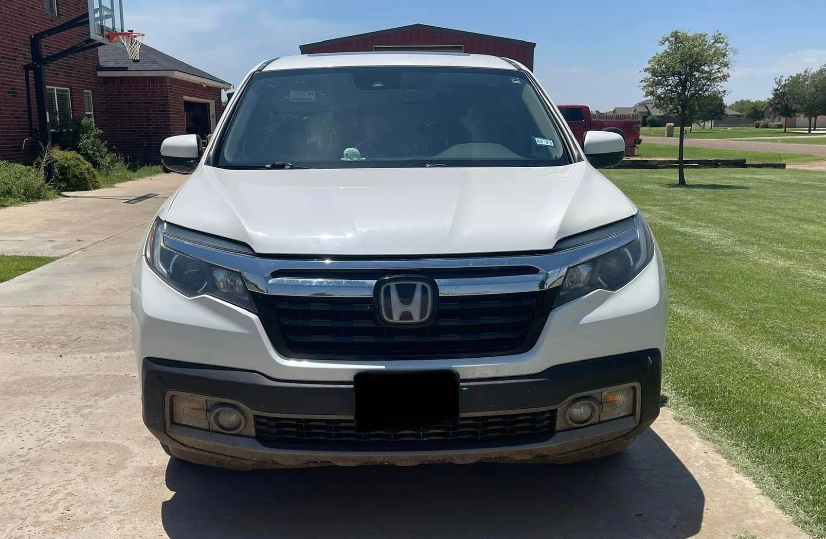 A white honda ridgeline is parked in a driveway next to a basketball hoop.