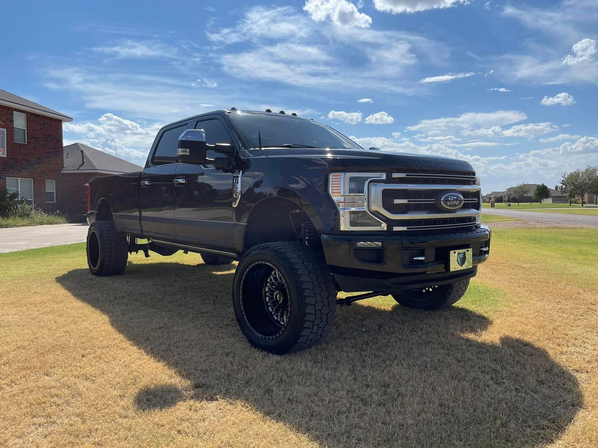 A black truck is parked in a grassy field in front of a house.