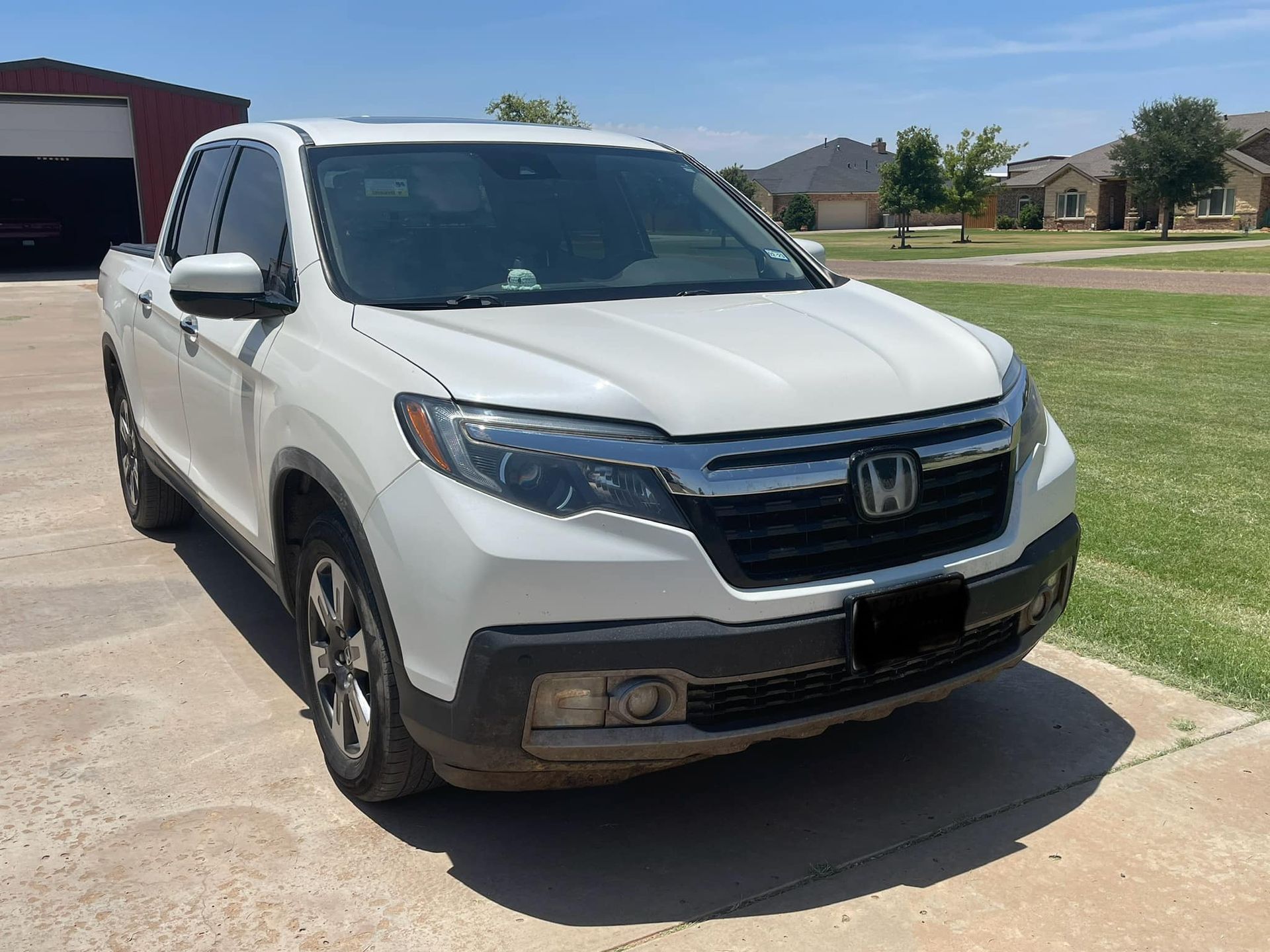 A white honda ridgeline pickup truck is parked in a driveway.