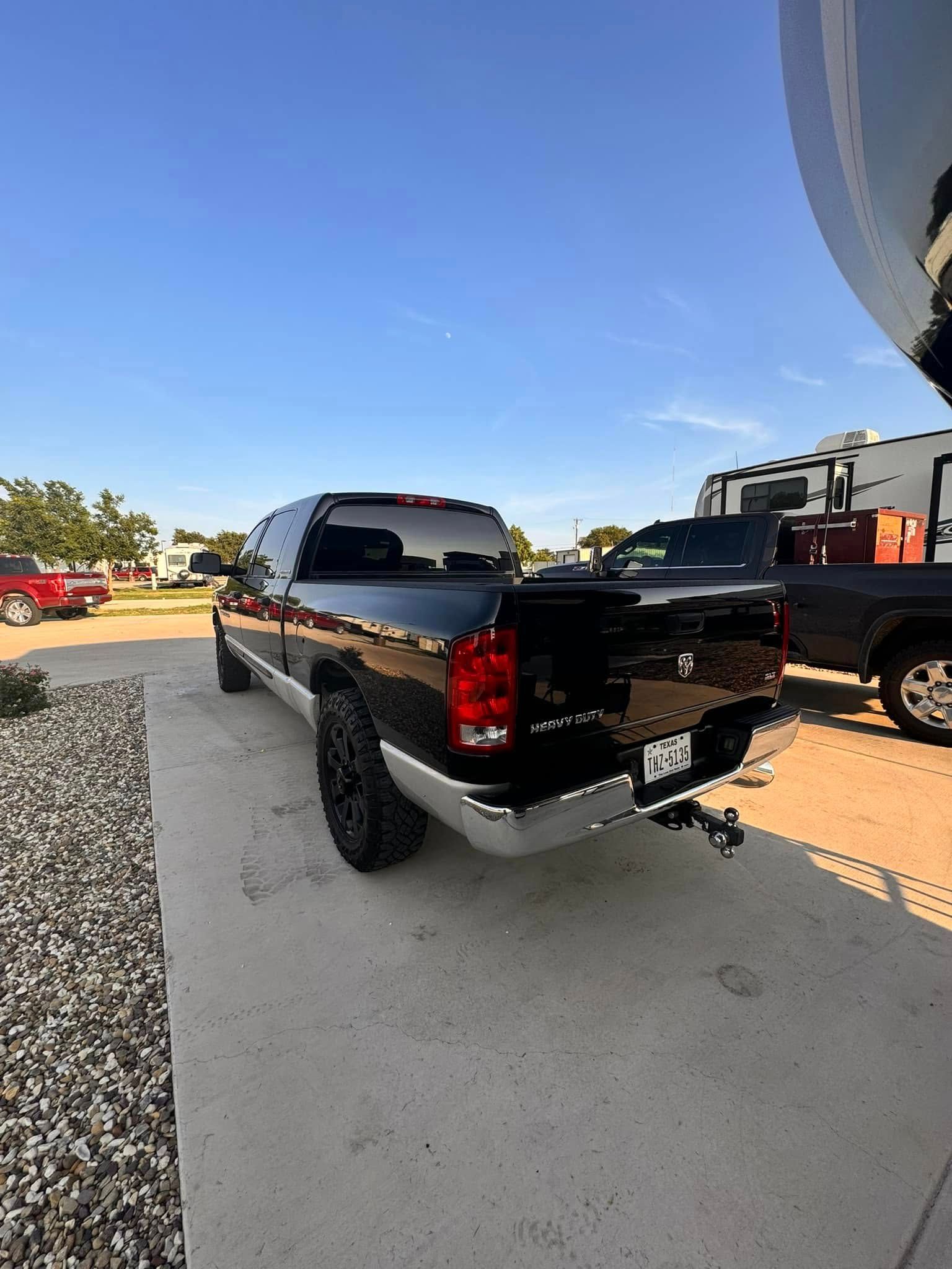 A black truck is parked in a parking lot next to a trailer.