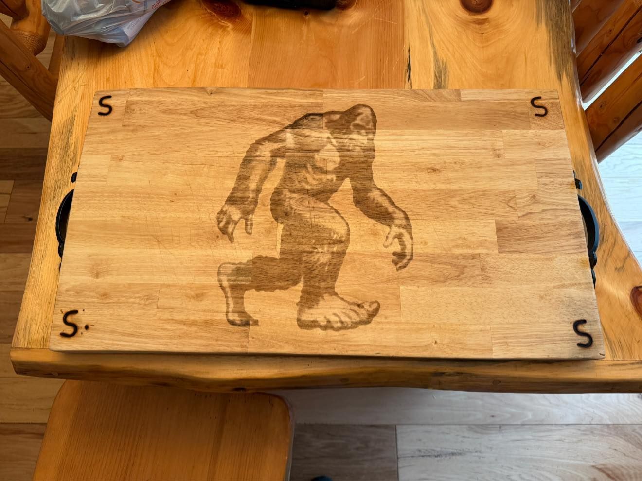 A wooden cutting board with a picture of a bigfoot on it is sitting on a wooden table.