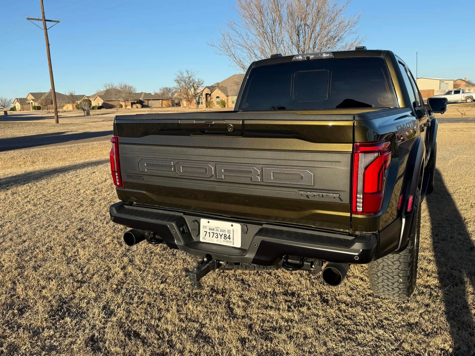The back of a ford raptor truck is parked in a field.