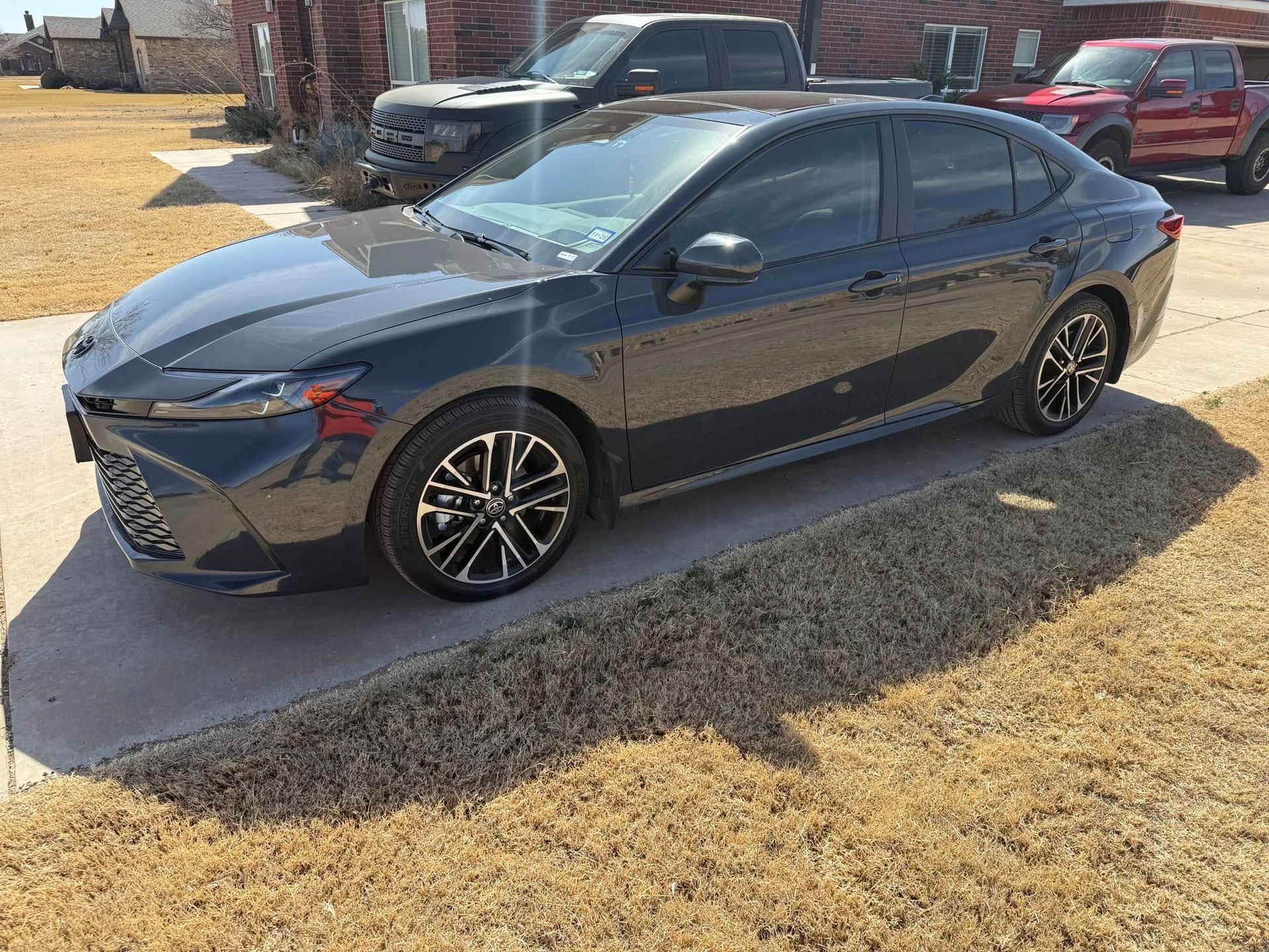 A black car is parked in a driveway next to a house.
