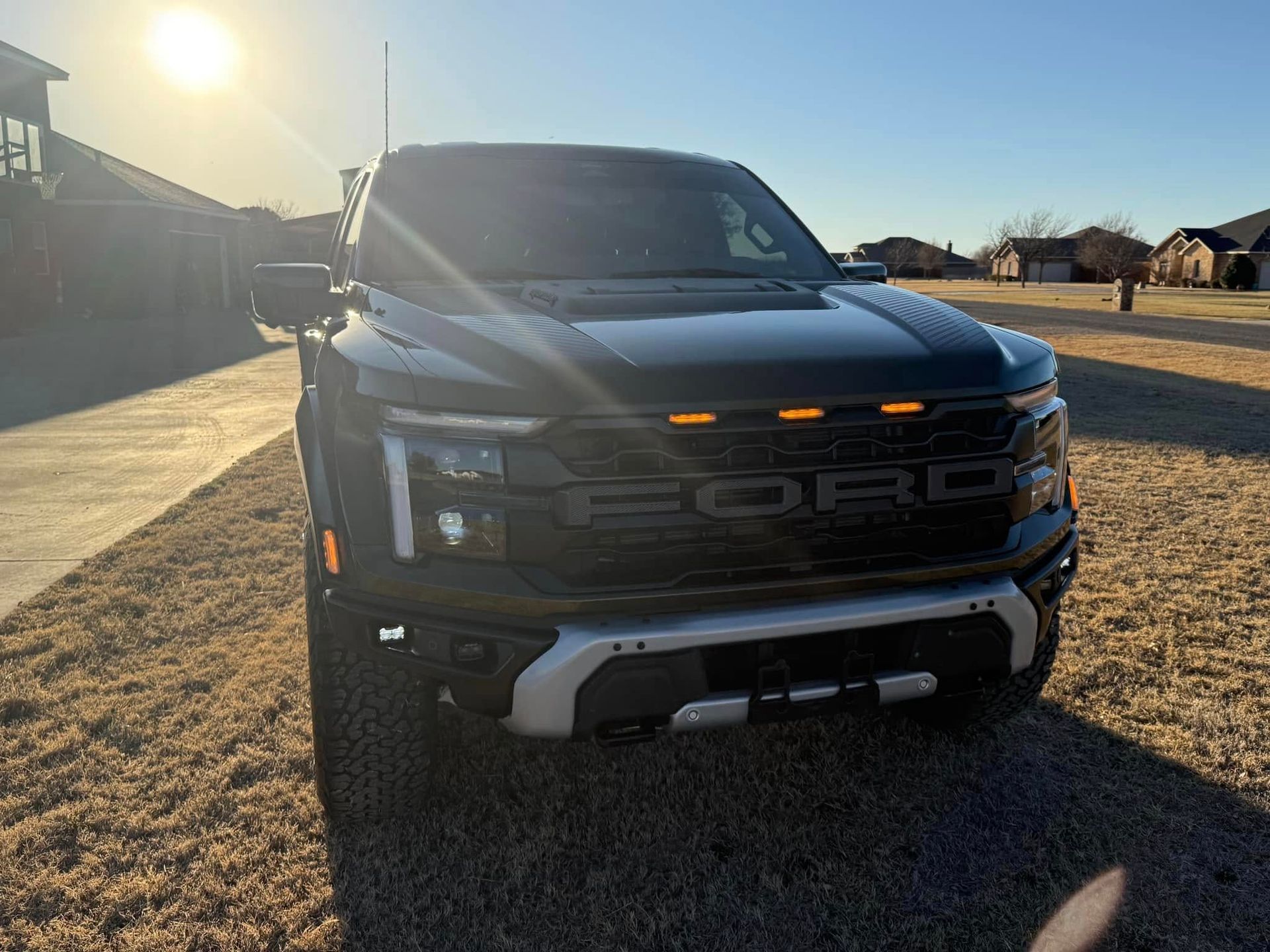 A black ford raptor truck is parked in a driveway.