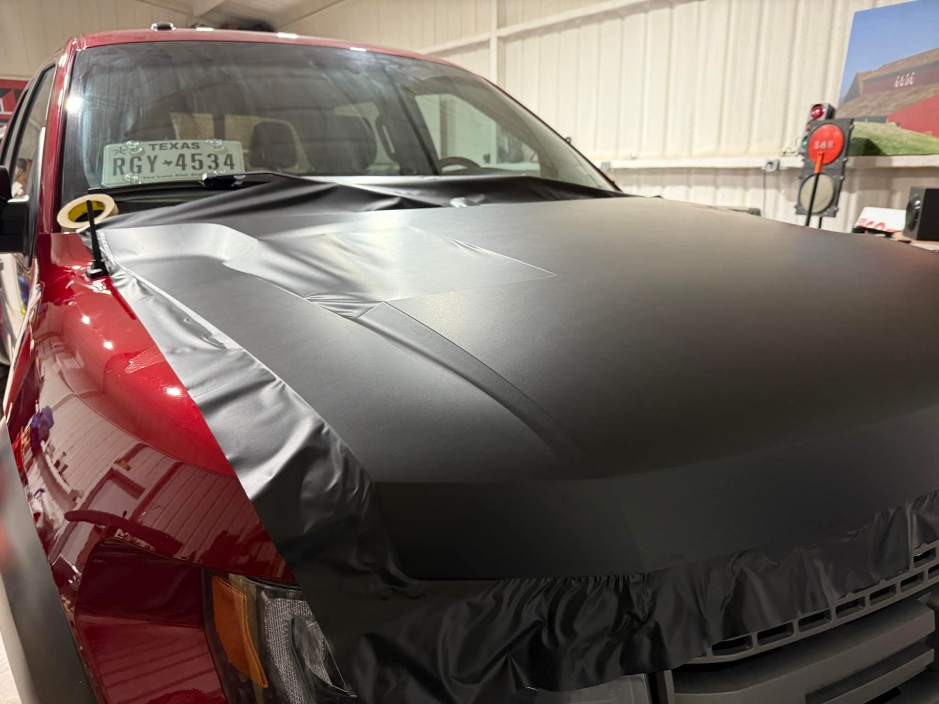 A red truck with a black hood is sitting in a garage.