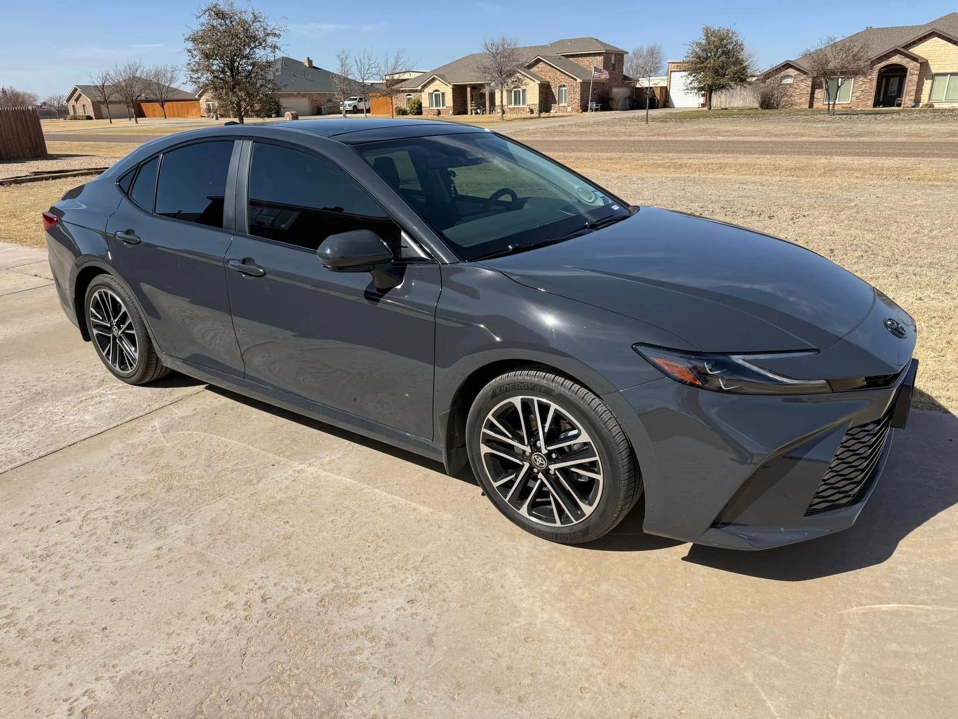 A gray toyota camry is parked in a driveway in front of a house.
