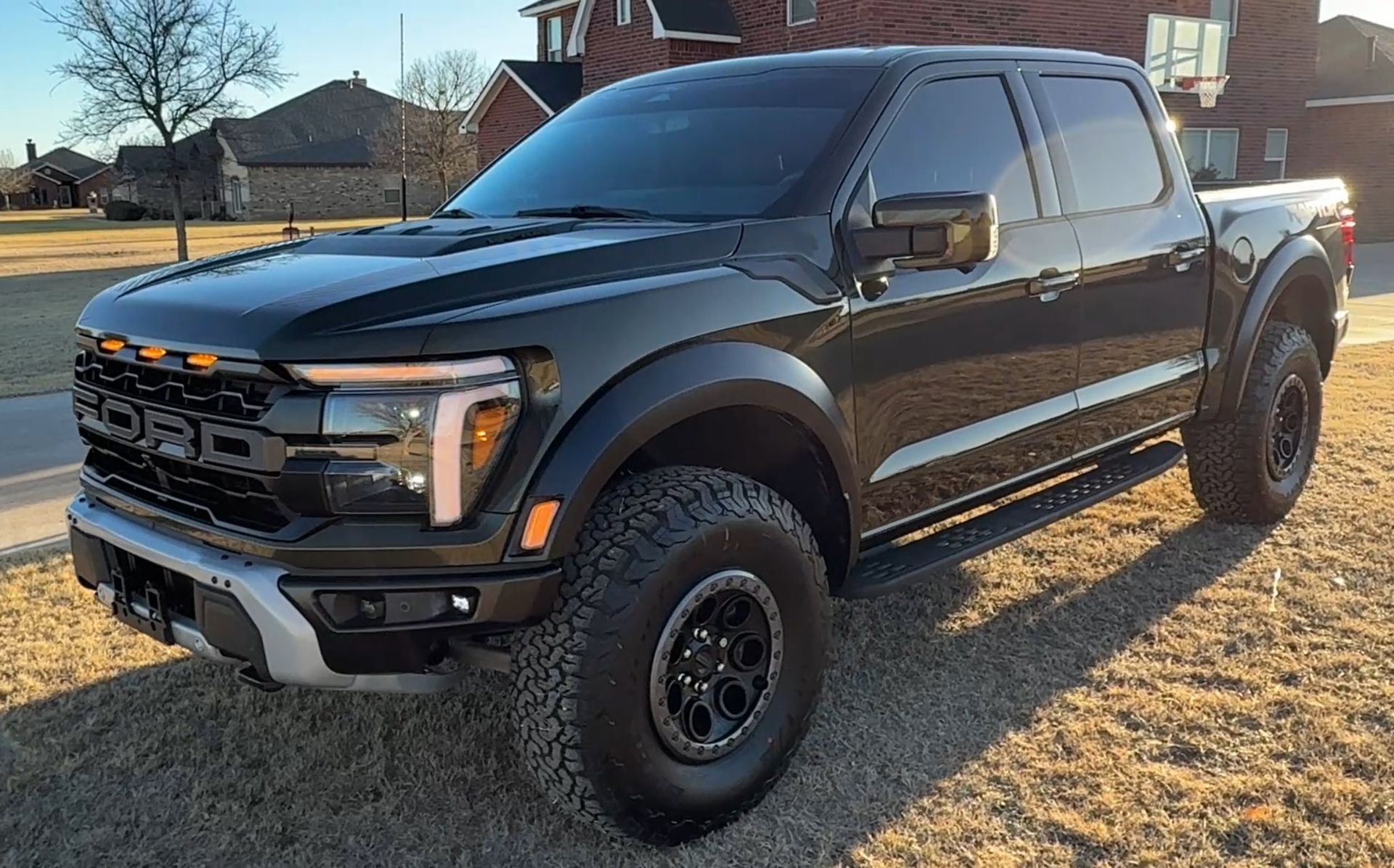 A black ford raptor truck is parked in front of a brick building.