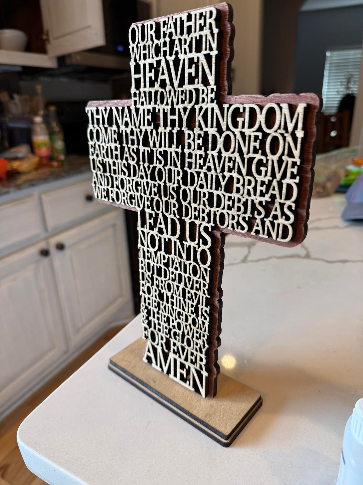 A wooden cross with the lord 's prayer on it is sitting on a counter.