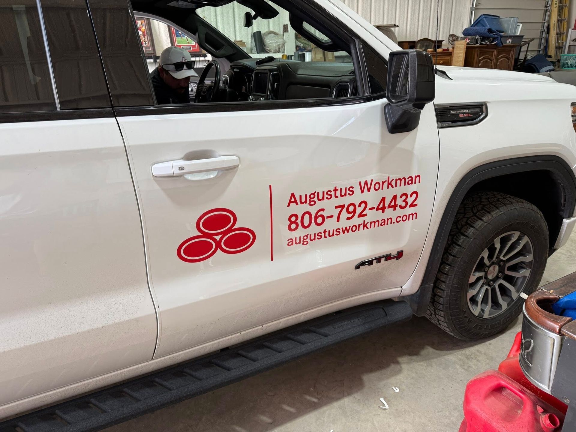 A white truck with a red logo on the side is parked in a garage.