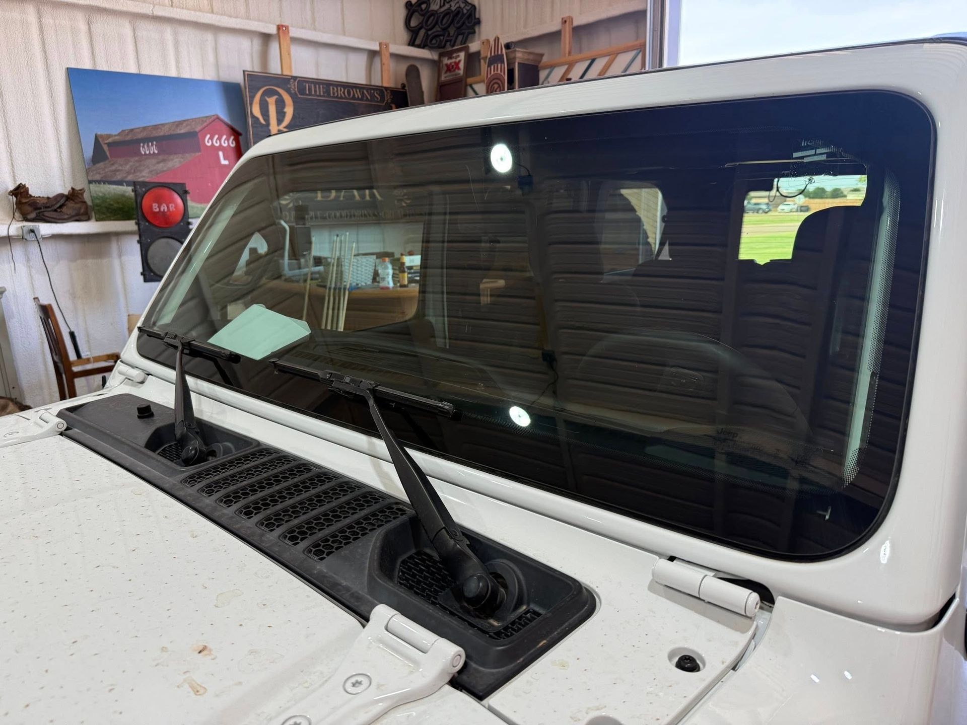 A white jeep is parked in a garage with the windshield open.