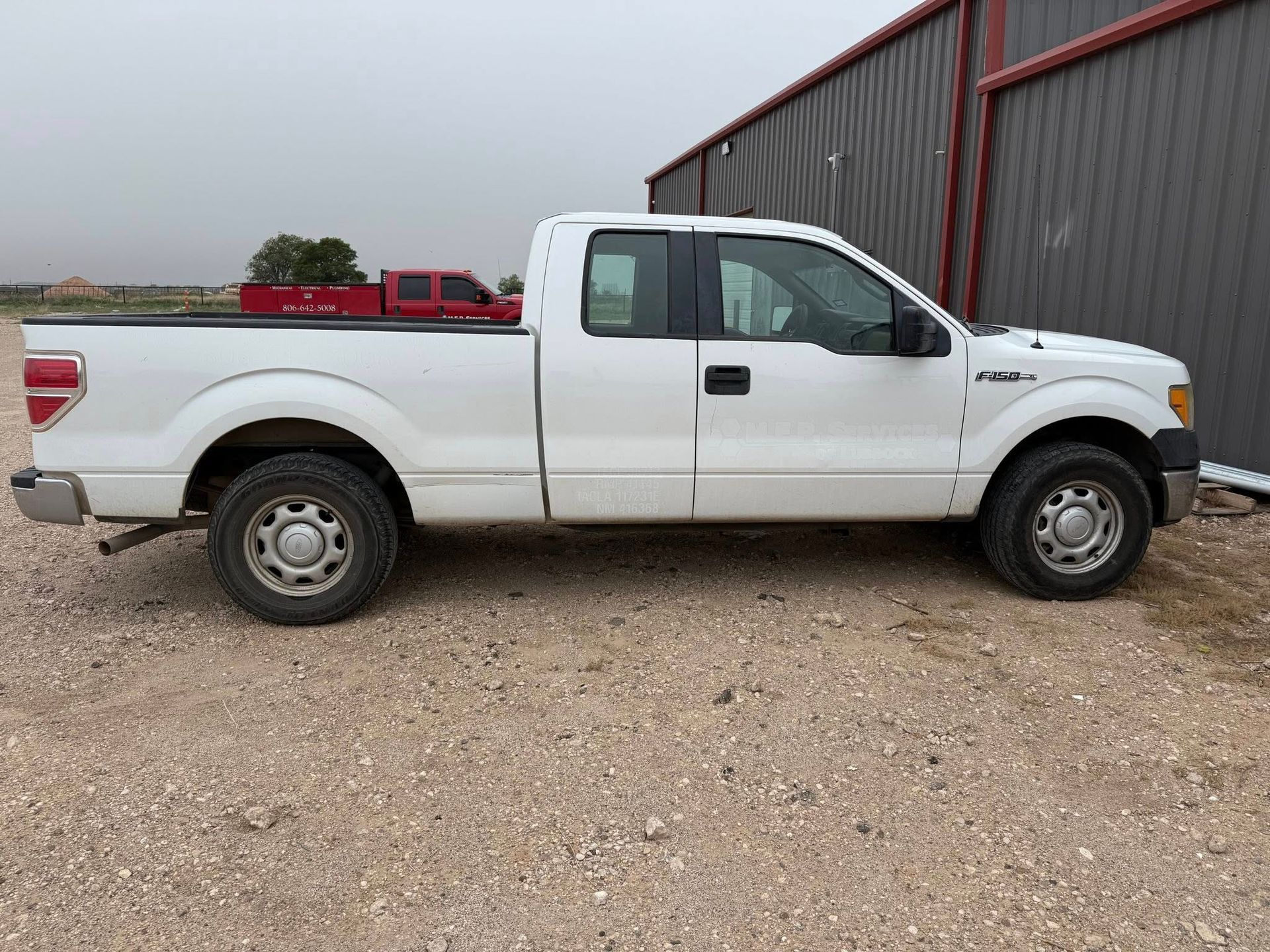 A white pickup truck is parked in a gravel lot in front of a building.