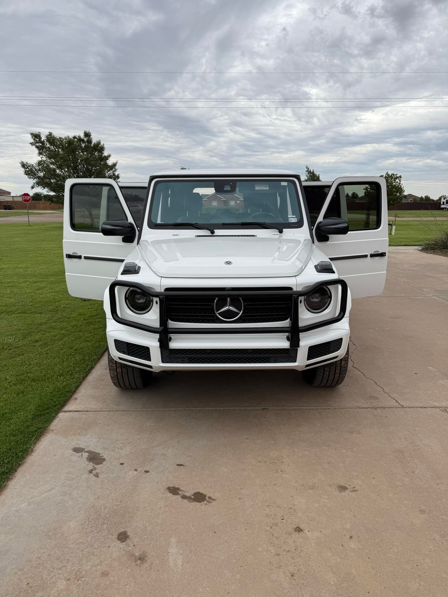 A white mercedes benz g class is parked on a driveway with its doors open.