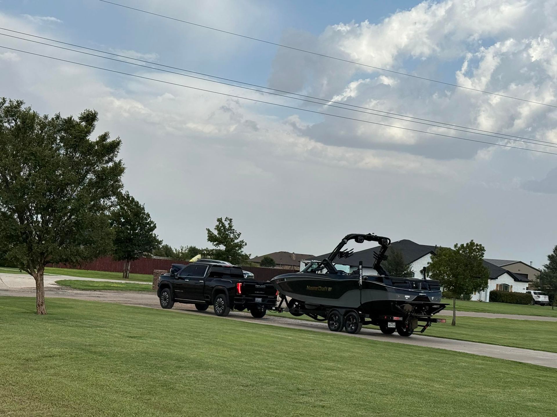 A black truck is towing a boat down a street.