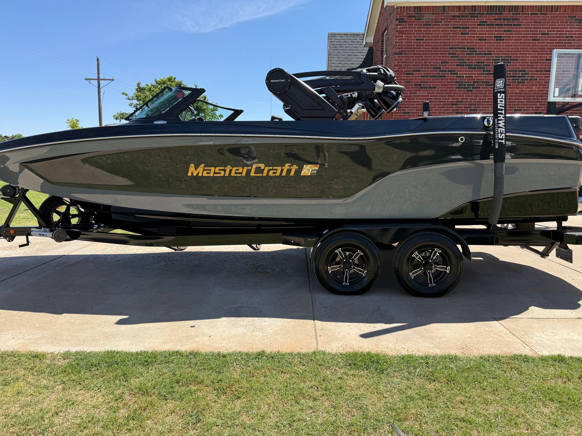 A black and gray MasterCraft boat on a trailer, parked on a paved surface in front of a red brick building.