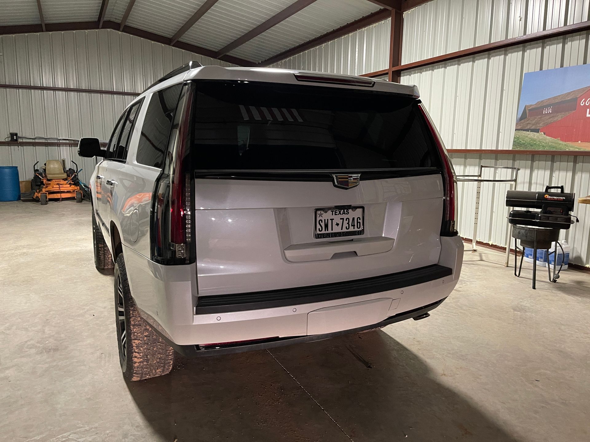 White Cadillac SUV parked inside a metal-roofed garage. Rear view, with a license plate visible.