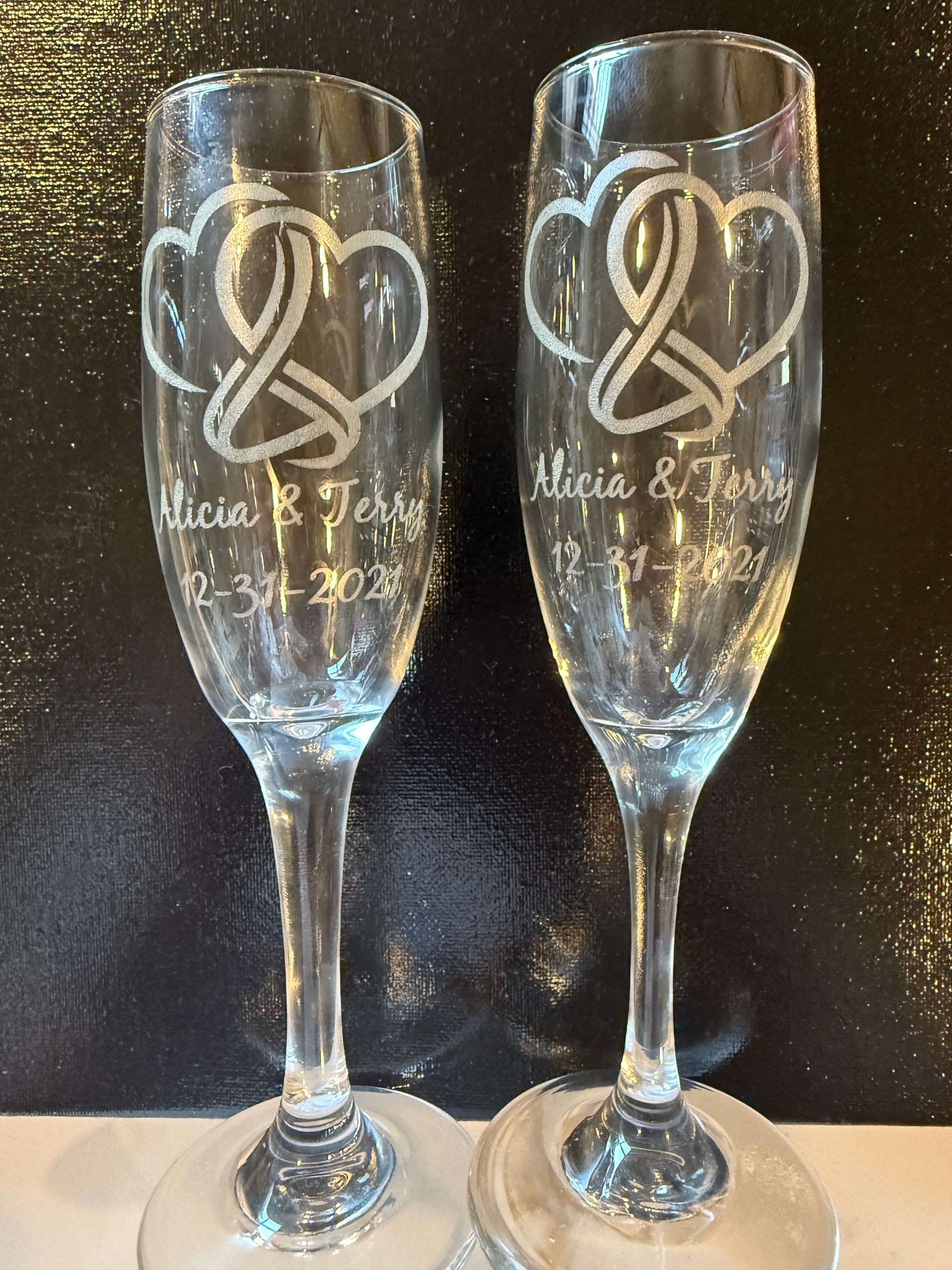 Two engraved champagne flutes with intertwined heart designs and names/wedding dates.