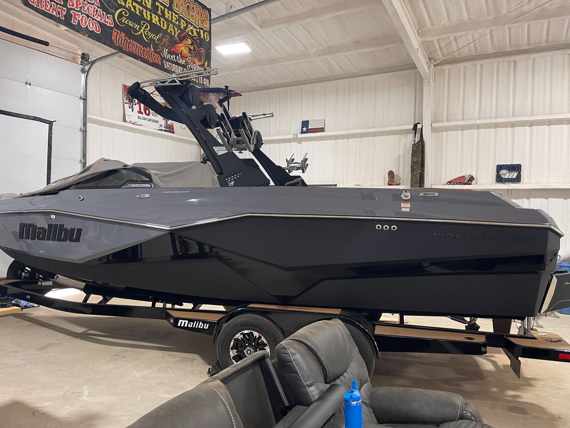 A dark gray Malibu wake boat on a trailer inside a garage, with the boat's tower raised.