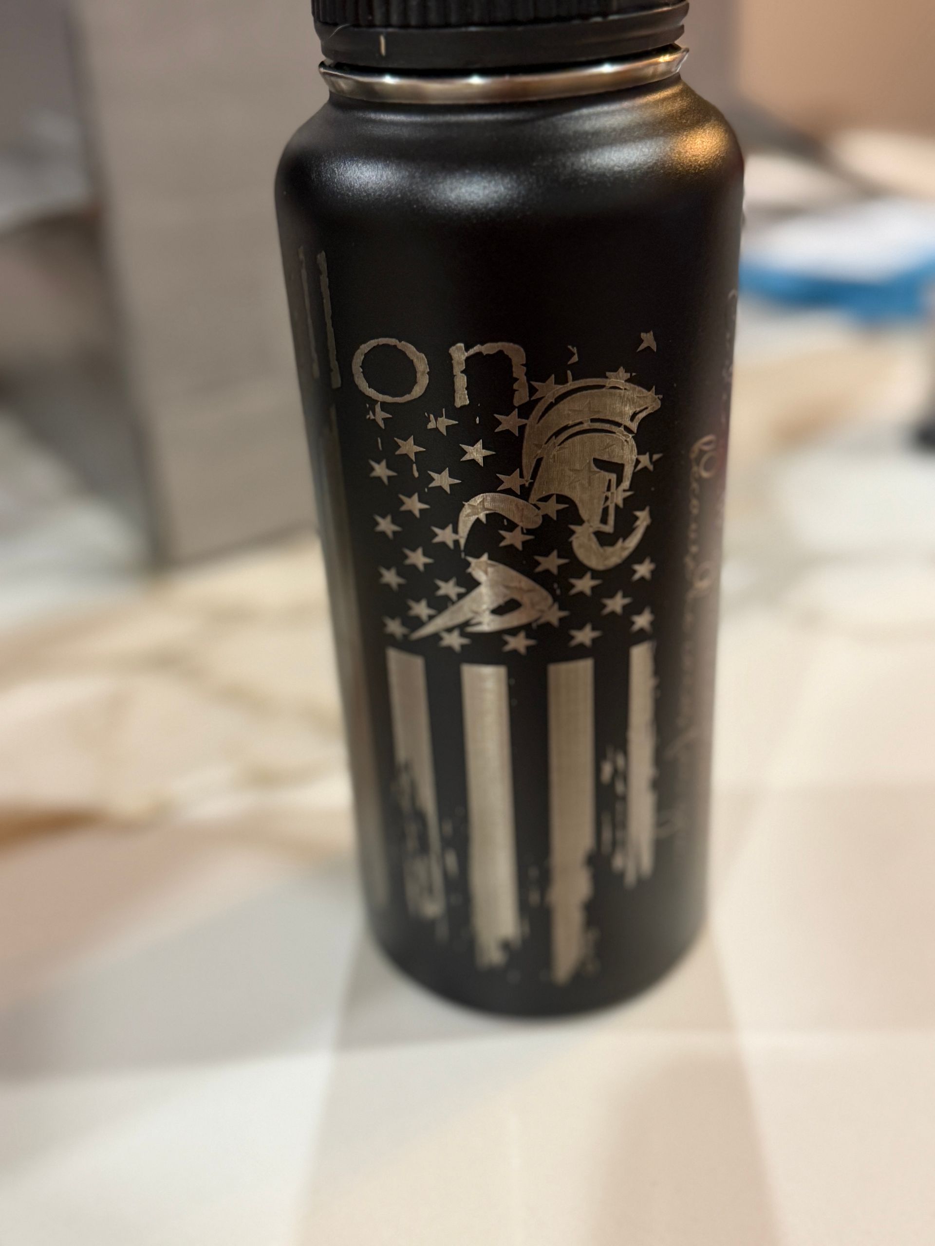 Black water bottle with engraved American flag and Spartan helmet design.