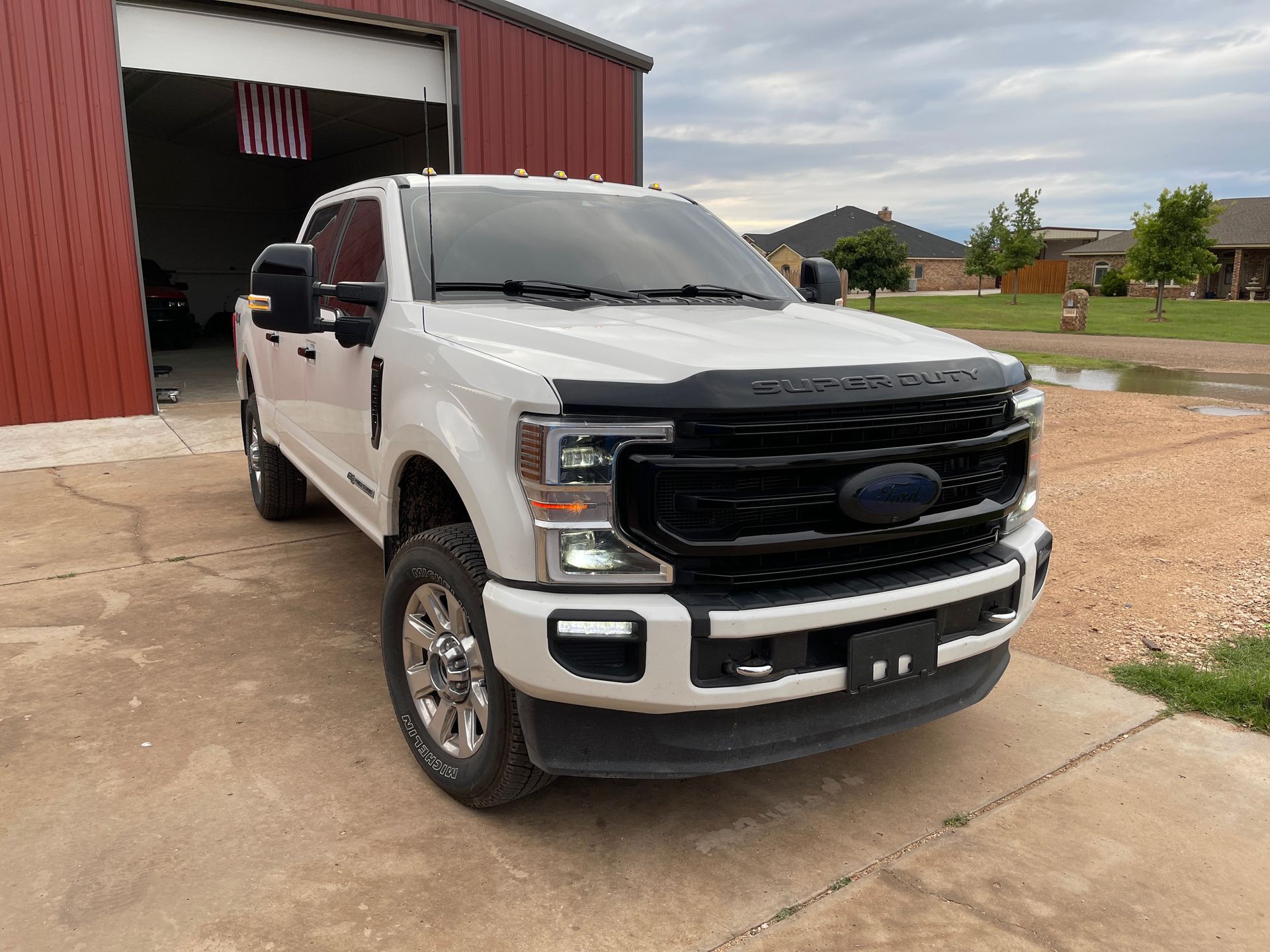 White Ford pickup truck parked in front of a red building with an American flag hanging inside. The sky is overcast.