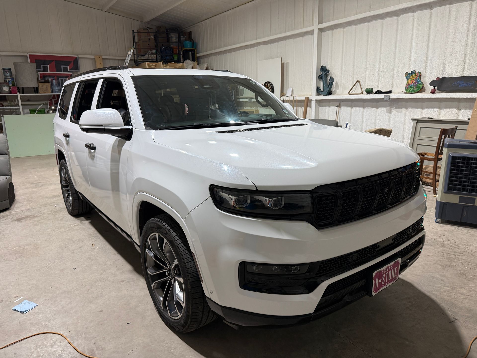 A white Jeep Wagoneer SUV with black grille, parked inside a garage. The vehicle is positioned at an angle.