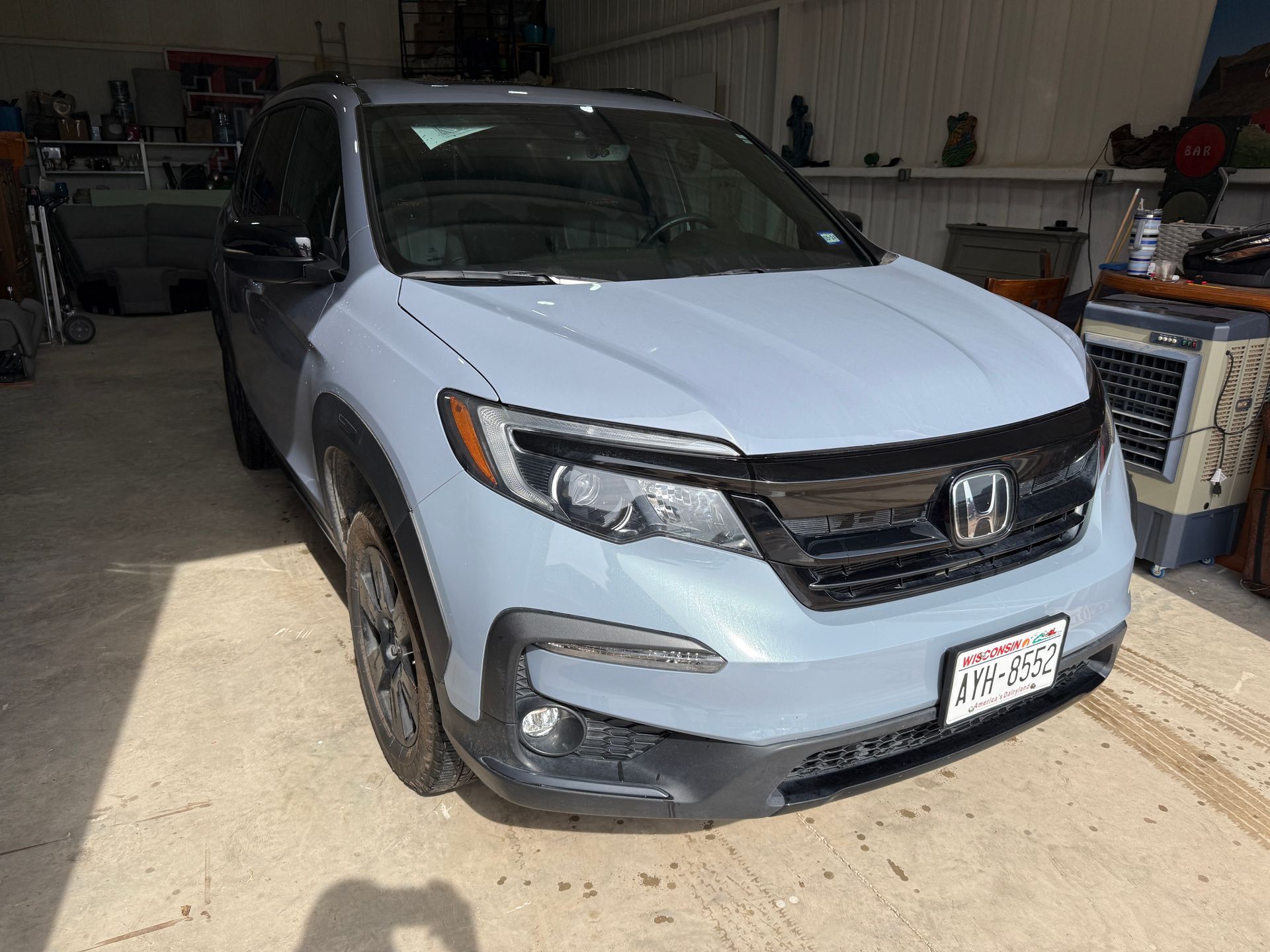 Gray Honda Pilot SUV parked in a garage with a Texas license plate, under bright sunlight.