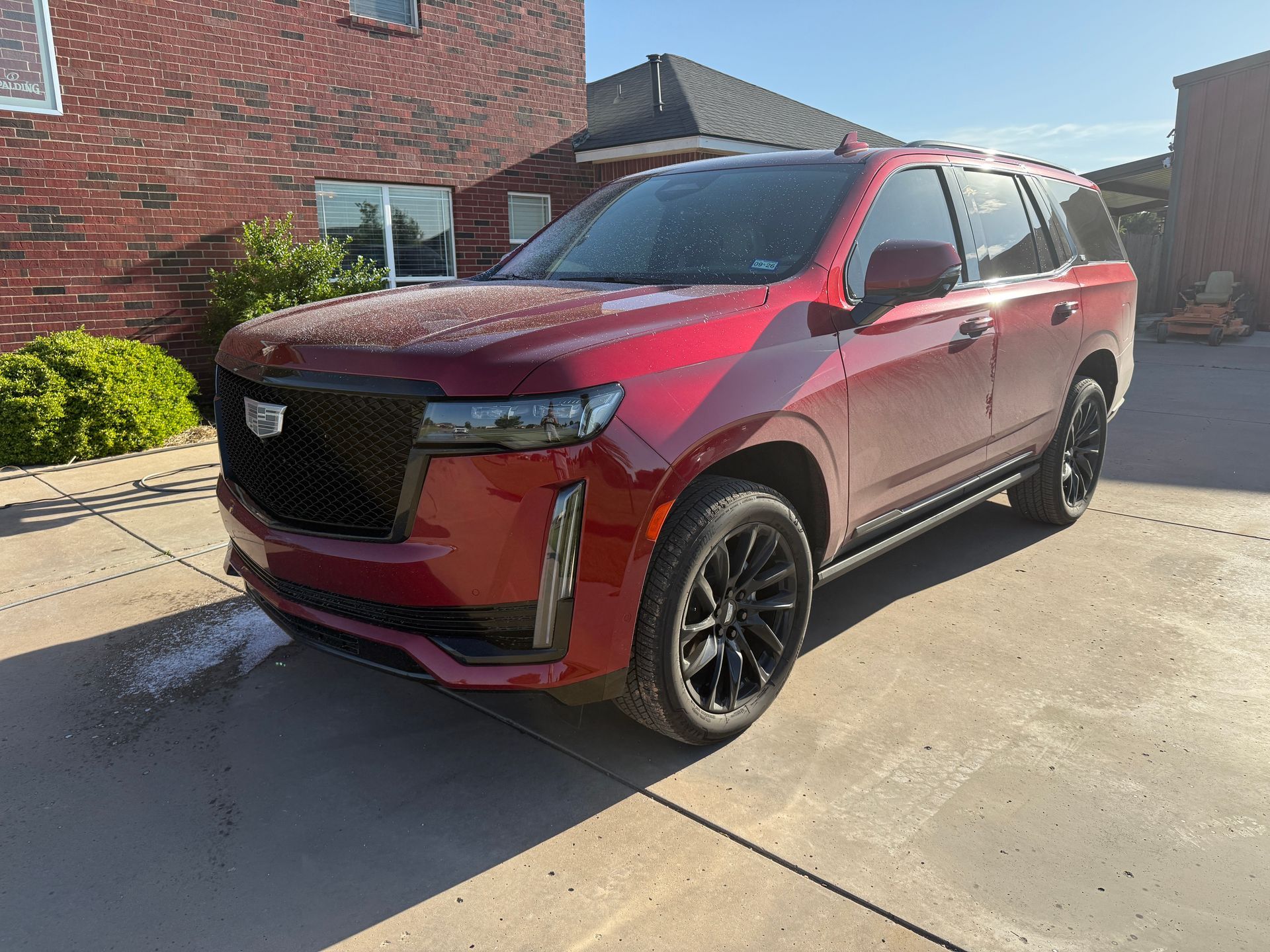 A red Cadillac Escalade parked in front of a brick building with black wheels.